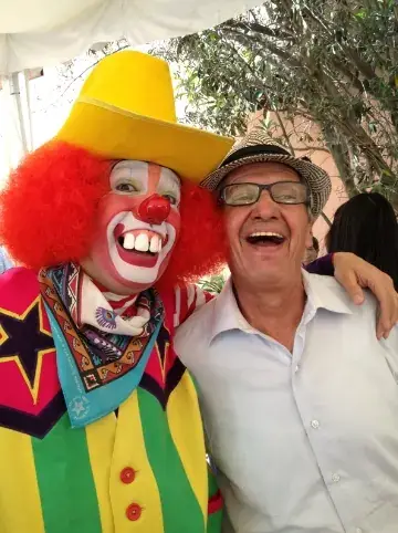 Payaso sonriente con sombrero amarillo posando con un invitado adulto en una fiesta