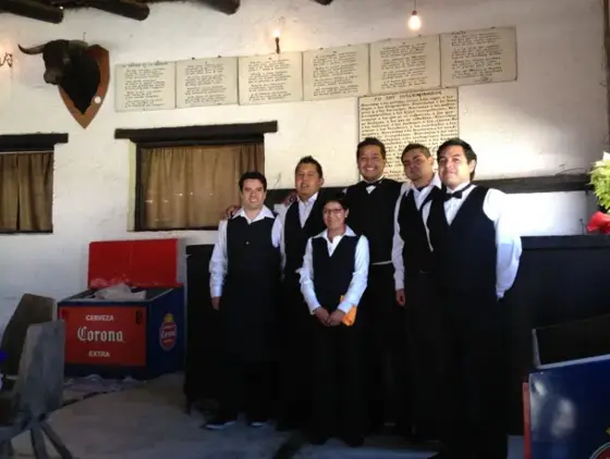 Meseros uniformados posando en un salón rústico
