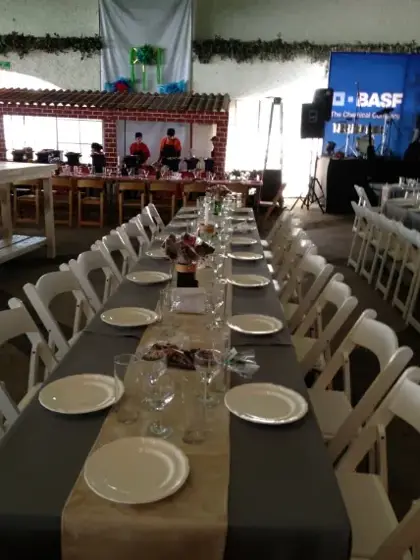 Mesas largas de banquete con vajilla y sillas blancas plegables