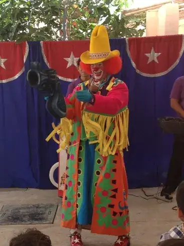 Payaso con traje colorido animando un evento sobre un escenario con fondo tricolor