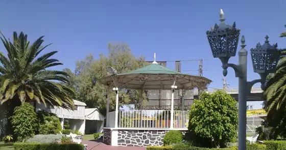 Kiosco con techo verde, palmeras y faroles en el jardín