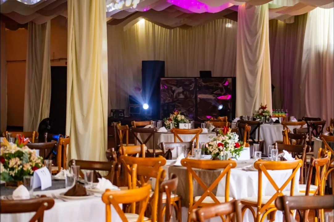 Salón con mesas redondas, sillas de madera, cortinajes claros y flores en el centro