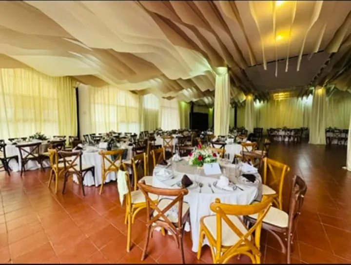 Salón amplio con mesas vestidas de blanco, sillas de madera y techo de telas onduladas