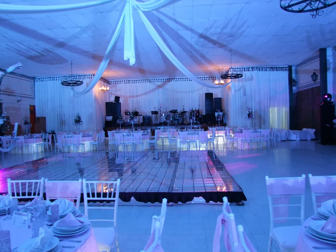 Salón con cortinajes blancos, pista de baile iluminada y escenario con instrumentos al fondo