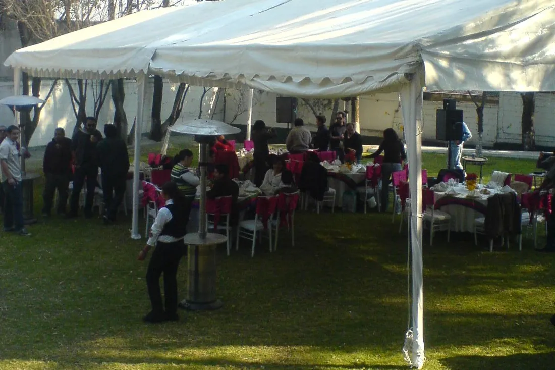 Jardín con carpa blanca, mesas con moños fucsia, calentadores y invitados