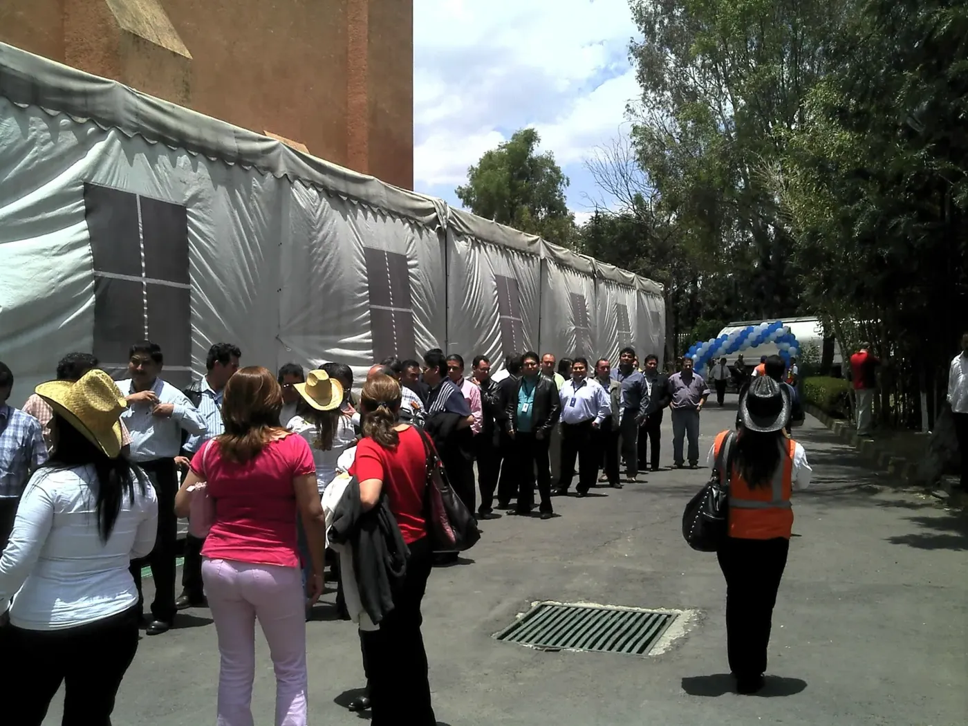 Carpa blanca de gran longitud con invitados formados a la entrada de un evento