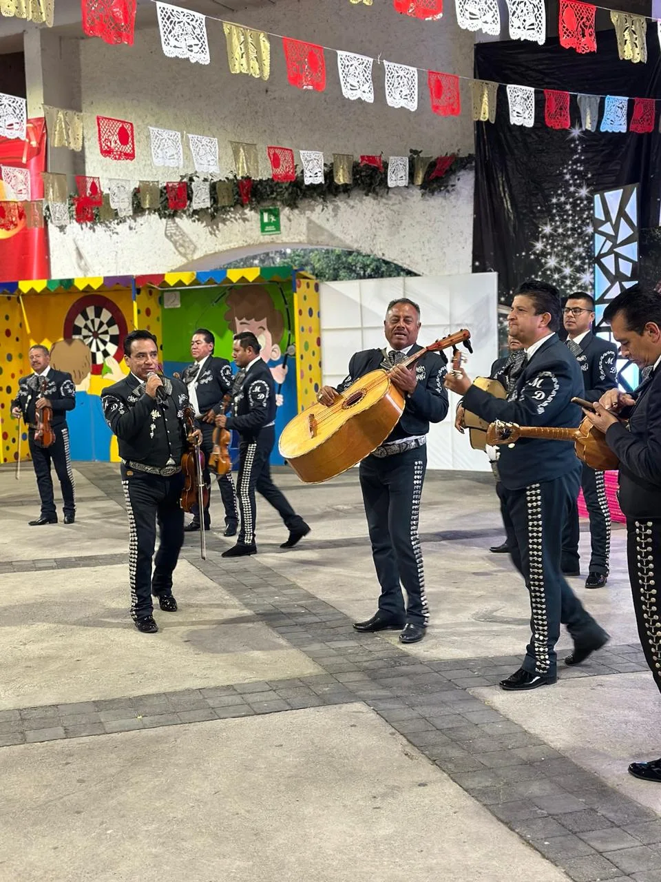Mariachi de traje negro con botonadura de plata tocando guitarrón y violines en una fiesta