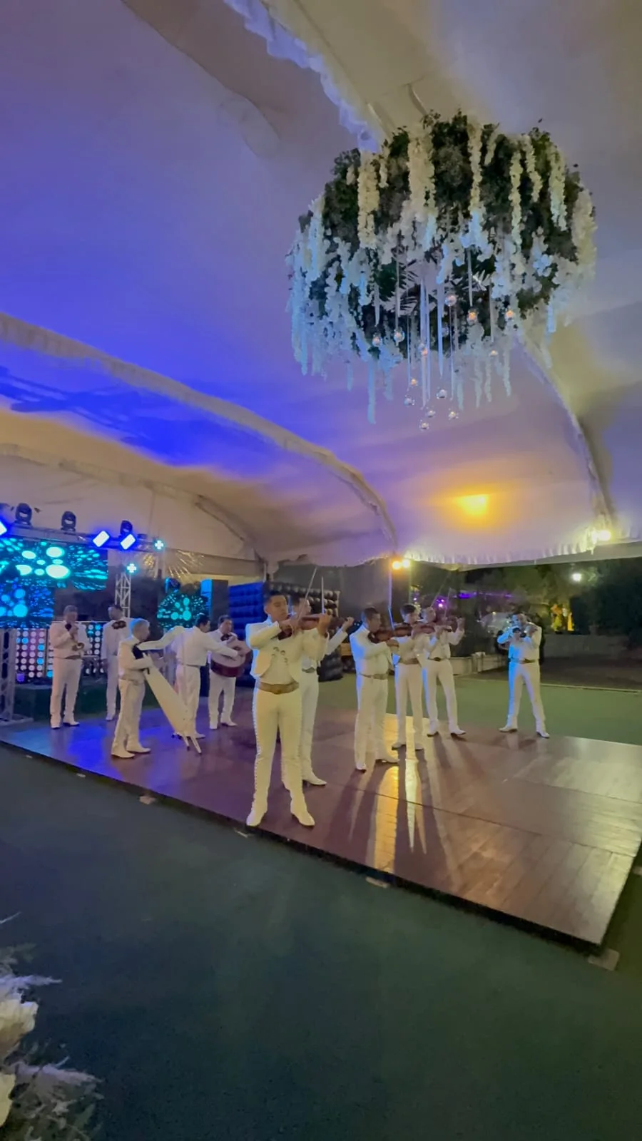 Mariachi de traje blanco tocando violines en una boda al aire libre bajo carpa