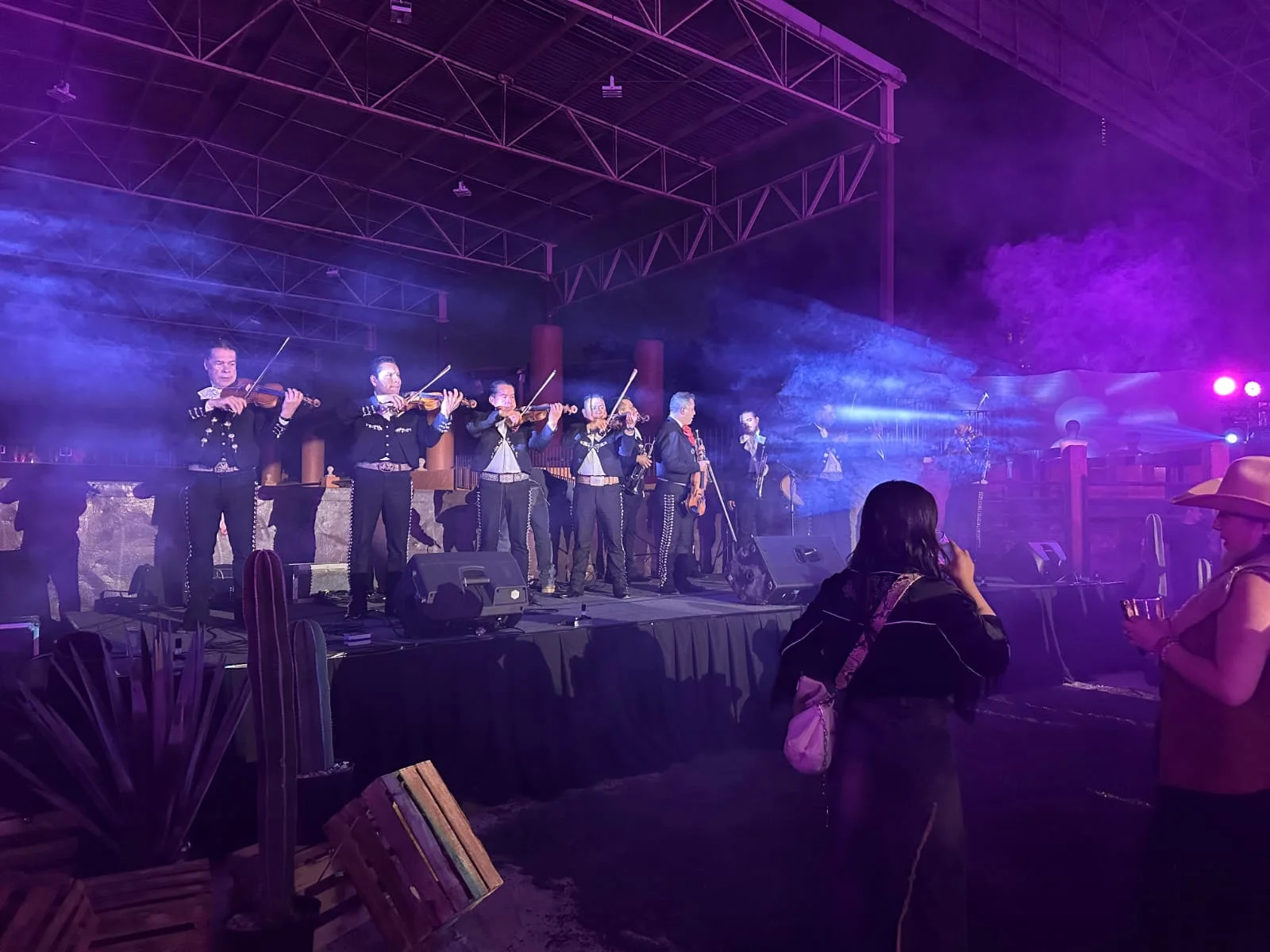 Mariachi tocando violines y trompetas sobre un escenario en un evento nocturno